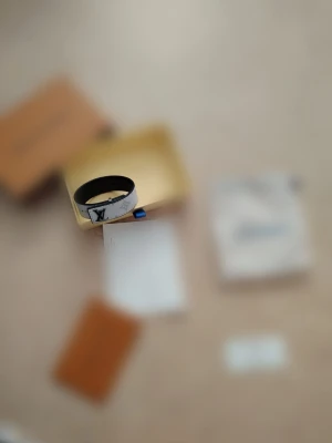  armband - Snyggt armband med klassiskt monogrammönster i grått och svart. Armbandet har en stilren design med metallspänne och är tillverkat i läder. Perfekt accessoar för att lyfta din outfit.