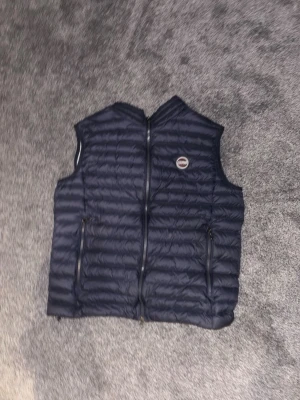 Mörkblå dunväst från Colmar - Snygg mörkblå dunväst från Colmar med quiltad design och dragkedja framtill. Västen har två praktiska fickor med dragkedja och en rund Colmar-logga på bröstet. Är i princip helt ny då jag köpte fel storlek som inte passade.