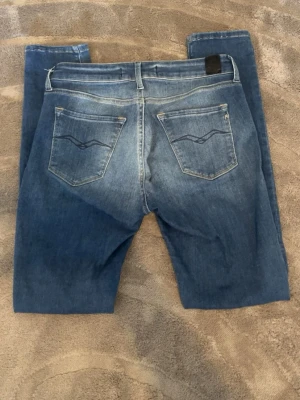 Blå slim fit jeans med broderade fickor - Snygga blå slim fit jeans med ljusa slitningar framtill och broderade bakfickor. Klassisk femficksmodell med normal midja och smala ben. Perfekta för en avslappnad och trendig look.