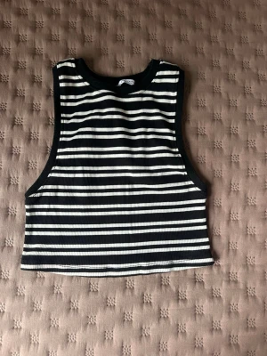 Randig croppad linnetopp från Zara - Snygg croppad linnetopp från Zara i svart och vitt med horisontella ränder. Toppen är ärmlös och har ribbad struktur, perfekt för en trendig och avslappnad stil. Passar till både jeans och kjol.