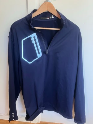 Ralph Lauren RLX tröja stl L mörkblå - Mörkblå RLX Ralph Lauren långärmad tröja i stl L med halv dragkedja fram. Har en bröstficka med dragkedja och tryckt RLX-logga bak i nacken.  Hör av er angående frågor! /Hugo