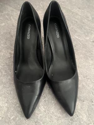 Svarta pumps från Even&Odd - Klassiska svarta pumps från Even&Odd med spetsig tå och smal klack. Skorna är tillverkade i ett slätt material som ger en stilren look. Perfekta för dig som gillar en tidlös och elegant stil.