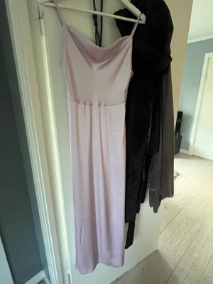 Ljuslila bal klänning i satin - Säljer en elegant ljuslila långklänning med tunna axelband och mjukt fall. Klänningen har en slät satinliknande yta och en enkel, stilren design som ger en lyxig känsla. Perfekt för dig som vill ha en feminin och trendig look. Använt en gång kostar orginalt runt 430