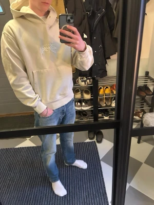 Beige hoodie från Stussy - Säljer en beige hoodie från Stussy i storlek s med vit logga på bröstet. Hoodien har huva, magficka och ribbade muddar vid ärmslut och nederkant. Perfekt för en avslappnad streetwear-look. Materialet känns mjukt och skönt mot huden. Obs, det finns en färg fläck på magfickan.