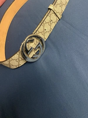 Bälte  - Snyggt beige bälte med GG-mönster och stor silverfärgad GG-spänne. Bältet är gjort i skinn och har känsla med detaljer i beige och brunt. Perfekt accessoar för att lyfta din outfit.