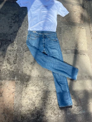 Levi's 501 blå raka jeans - Klassiska blå jeans från Levi's med rak passform och fem fickor. Jeansen har en tidlös look med normalhög midja och är tillverkade i denim. Perfekta för en avslappnad och stilren outfit.