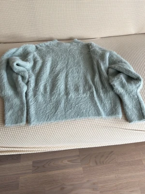 Ljusgrön fluffig stickad tröja - Supermjuk och fluffig ljusgrön stickad tröja med rund hals och långa ärmar. Perfekt för dig som gillar en avslappnad och cozy stil. Tröjan har en lös passform och är tillverkad i ett lurvigt material som känns extra gosigt.