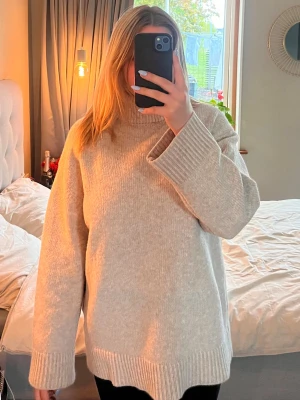 Beige oversized stickad polotröja - Mysig beige stickad polotröja med oversized passform och breda ribbade muddar vid ärmslut och nederkant. Tröjan har hög krage och är perfekt för lager-på-lager-stil under kyliga dagar. Enkel och stilren design som passar till det mesta.