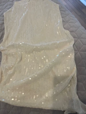 Champagnefärgad paljettklänning FB Sister - Champagnefärgad kort klänning från FB Sister, täckt med glittriga paljetter. Ärmlös modell med rund halsringning och dragkedja bak. Perfekt för dig som vill sticka ut med en glittrig look.