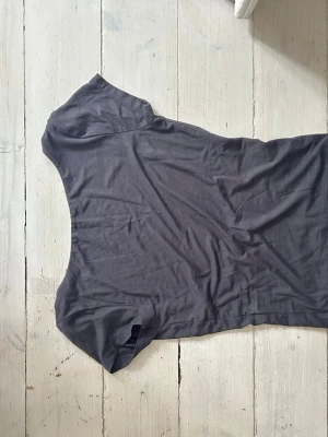 Mörkgrå topp med öppen rygg - Snygg mörkgrå topp i bomull med korta ärmar och en djup, öppen rygg. Enkel och stilren design som passar perfekt till jeans eller kjol. Skön och mjuk känsla mot huden.