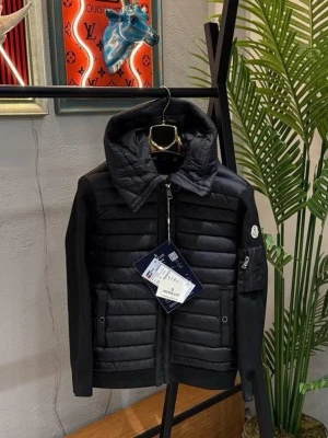 Svart pufferjacka från Moncler - Snygg svart pufferjacka från Moncler med quiltad front och rygg, stickade ärmar och stor huva. Jackan har dragkedja framtill, fickor med knappar och Moncler-logga på ärmen. Perfekt för kalla vinterdagar och ger en stilren look.