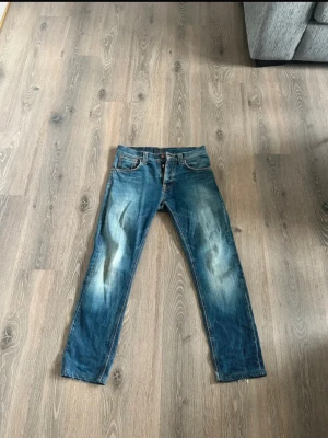 Nudie Jeans Steady Eddie - Säljer ett par klassiska blå jeans från Nudie Jeans, modellen Steady Eddie. Jeansen är tillverkade i 100% ekologisk bomull och har en snygg tvätt med slitningar på benen. Passformen är rak och de har fem fickor samt orangea sömmar. Väldigt bra skick, snygga fades och har möjlighet att bli ännu snyggare. W30 L32 sitter mer som L30