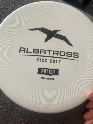 Albatross Disc Golf Putter - Vit discgolf-putter från Albatross med svart logga och text. Tillverkad i plast och godkänd av PDGA. Rund form med räfflad kant för bättre grepp. Perfekt för discgolfbanan.