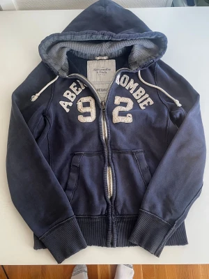 Abercrombie & fitch zip hoodie mörkblå (eftertraktad) - Riktigt snygg och eftertraktad Abercrombie zip hoodie. fint skick inga fel storlek M kan även passa S kan ta mått vid behov. Endast 438kr ej hugget i sten kom gärna med frågor och prisförslag har även mycket mer liknande i min profil alla storlekar kolla gärna stor rabatt vid köp av flera 😁✌️