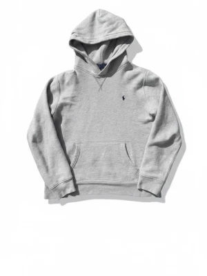 Grå hoodie från Polo Ralph Lauren - Klassisk grå hoodie från Polo Ralph Lauren med broderad logga på bröstet. Hoodien har huva, känguruficka och ribbade muddar. Tillverkad i mjuk bomullsblandning som är skön att ha på sig.