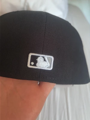 Svart MLB keps från New Era - Snygg svart fitted keps från New Era med MLB-logga broderad bak. Klassisk modell med böjd skärm och detaljerad insida med New Era-band. Perfekt för dig som gillar sportig streetstyle och vill ha en stilren accessoar. Pris kan diskuteras! Säljer för den är för stor 