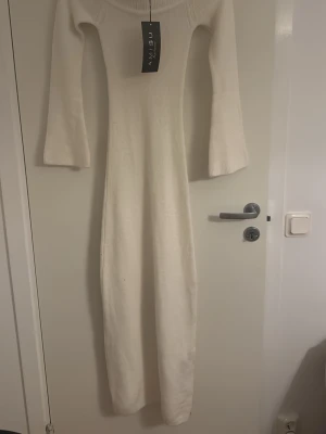 Vit lång stickad klänning - Långärmad, vit stickad klänning från New Yorker med figurnära passform och rund hals. Klänningen är golvlång och har en mjuk, stretchig känsla som passar perfekt till kyligare dagar.