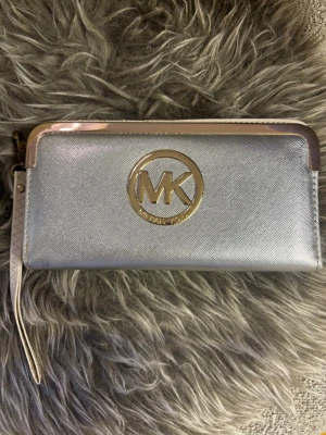 Silverfärgad plånbok Michael Kors - Snygg silverfärgad plånbok från Michael Kors med guldfärgad logga framtill. Köpt på Busfrö/ Secondhand så vet ej om den är äkta!