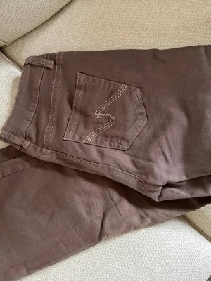 Bruna bootcut jeans med broderad ficka & låg midja - Snygga bruna jeans med bootcut passform och coolt broderi på bakfickan. Jeansen har klassisk femficksdesign och är tillverkade i ett mjukt bomullstyg som känns skönt mot huden. Perfekta för en avslappnad och trendig look. Low waist.