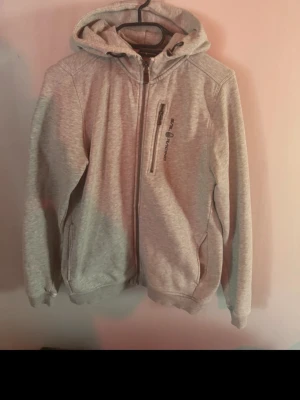 Sail racing hoodie  - Grå hoodie från Sail Racing med dragkedja framtill, bröstficka med zip och logga på bröstet. Perfekt för chill dagar eller när du vill vara bekväm och snygg. 
