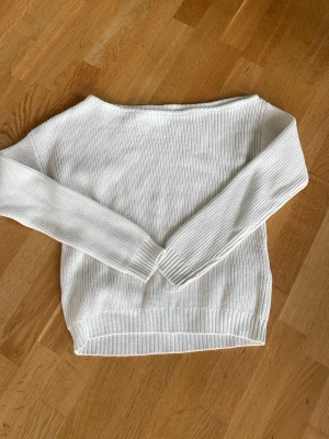 Vit stickad tröja off shoulder - Klassisk vit off shoulder stickad tröja medlånga ärmar. Tröjan har ribbade muddar vid ärmslut och nederkant, och är tillverkad i ett mjukt, tunt material som passar perfekt till sommaren. Enkel och stilren design som funkar till det mesta. Den är från even and odd!