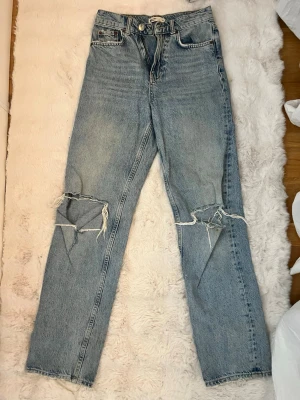 Blå mom jeans med slitna knän - Säljer ett par ljusblå mom jeans med hög midja och raka ben från ginatricot. Tyvärr har de fått en fläck vid knät, se bild. 