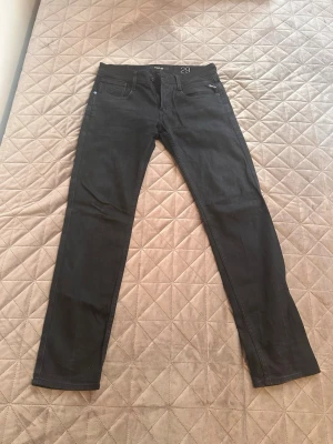 Svarta slim fit jeans från Replay - Säljer ett par svarta slim fit jeans från Replay. Klassisk femficksmodell med diskret Replay-logga vid fickan. Jeansen har raka ben och är tillverkade i ett mjukt denimtyg som sitter snyggt och bekvämt. Perfekta för en stilren och modern look.