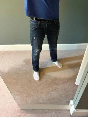Slim fit jeans med slitningar - Säljer ett par mörkblå jeans med slitningar och hål på både lår och knän. Jeansen har en smal passform och klassisk femficksdesign. Perfekta för dig som gillar en avslappnad och trendig stil. 