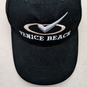 Svart keps med broderi Venice Beach - Svart keps med böjd skärm och broderad logga samt texten 'Venice Beach' framtill. Kepsen har klassisk passform och är tillverkad i bomullsmaterial. Perfekt accessoar för en avslappnad stil. Jag har tvättat den förhand 1 gång 
