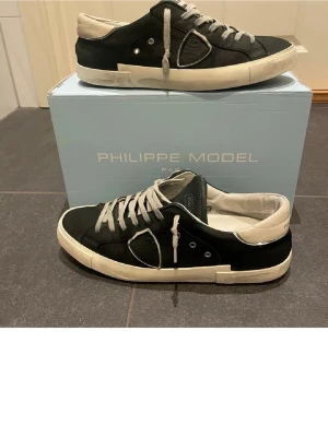 Philippe Model  - Snygga svarta sneakers från Philippe Model med vita detaljer och grå skosnören. Skorna har en låg silhuett, vit sula och är tillverkade i läder med mockadetaljer. Klassisk design pris går att diskutera.