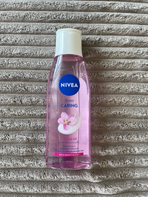 NIVEA Caring Toner med mandelolja - Fräsch ansiktstoner från NIVEA med mandelolja, speciellt framtagen för torr och känslig hud. Tonern är rosa och kommer i en genomskinlig plastflaska med vit kork och en söt blomdetalj på etiketten. Perfekt för att återfukta och lugna huden.