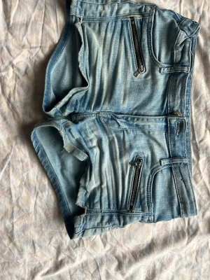 Ljusblå denimshorts med dragkedjor - Säljer ett par ljusblå denimshorts från IC DENIM med två framfickor med dragkedjor och två bakfickor. Shortsen har en klassisk femficksdesign och är tillverkade i bomull. Perfekta för sommaren och har en snygg, casual look.