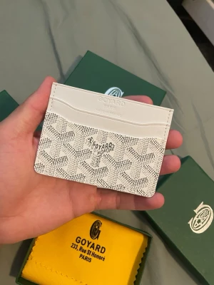 Korthållare - Snyggt och stilrent vitt korthållare med klassiskt mönster och flera fack för kort. Tillverkad i exklusivt skinn och levereras med originalask, gul putsduk och äkthetskort. Perfekt accessoar för dig som gillar lyxiga detaljer.