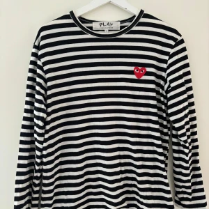 Randig långärmad tröja från Comme des Garçons - Säljer en superfin randig tröja från Comme des Garçons med deras ikoniska röda hjärta på bröstet. Den är i bra skick och väldigt bekväm att ha på sig. Storlek L men passar mig som vanligtvis har S.