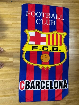 Barcelona FCB filt i blått och rött - Mysig filt med FC Barcelonas klassiska klubbmärke och texten 'FOOTBALL CLUB BARCELONA'. Färgerna är blå och röd med gula detaljer och svartvit text. Perfekt för att chilla hemma eller ta med till soffan under matchkvällar.