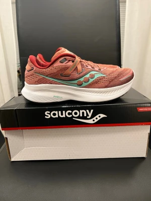 Saucony Guide 16 Soot/Sprig , EUR 38 - Snygga sneakers från Saucony i en aprikos  nyans med turkosa och vinröda detaljer. Ovandelen är i mesh för bra andningsförmåga och sulan är vit och tjock för extra komfort. Perfekta för dig som gillar sportig stil och vill ha något som sticker ut.      ****använd endast ett gång på grund av fel storlek