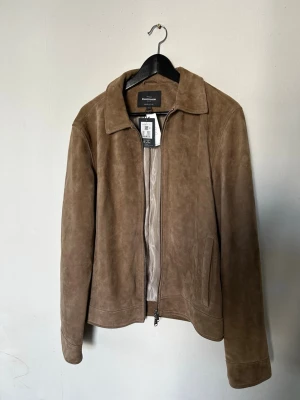 Äkta Mockajacka  - Snygg brun mockajacka från Double A med klassisk krage och dragkedja framtill. Jackan har två sidfickor och en stilren, minimalistisk design. Perfekt för dig som gillar en clean och tidlös look. Jackan är totalt ny, och helt oanvänd med orginaltags. Kvitto finns även. Pris går att förhandla