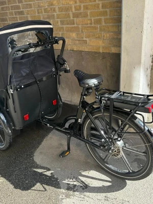 Cargobike Flex 2025  - Säljer en svart eldriven lådcykel med stort lastutrymme framtill, perfekt för att transportera barn eller packning. Cykeln har robust ram, bekväm sadel och pakethållare bak. Utrustad med skivbromsar och batteri monterat under pakethållaren. Stilren och praktisk design. Cykeln säljs med alla tillbehör som nycklar batteri laddare kapell och kvitto. 