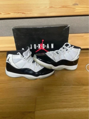 Air Jordan 11 Concord Highs - Säljer ett par ikoniska Air Jordan 11 Concord med svart och vit färgkombination, högt skaft och blankt lackläder runt om. Skorna har Jumpman-loggan på sidan och siffran 45 på hälen. Klassisk siluett och riktigt snygga detaljer för dig som gillar sneakers.