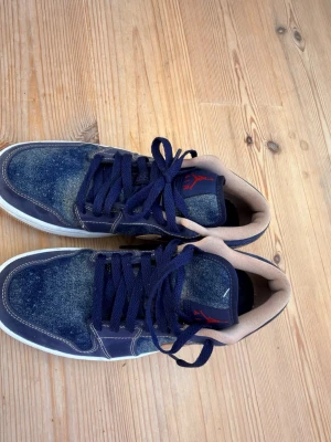 Blåa Air Jordan mids med mockadetaljer - Säljer ett par blåa Air Jordan sneakers med mörkblå mockadetaljer, vita sulor och beige insida. Skorna har klassisk Jordan-logga i rött på plösen och mörkblå skosnören. Perfekta för dig som gillar streetwear och vill sticka ut.