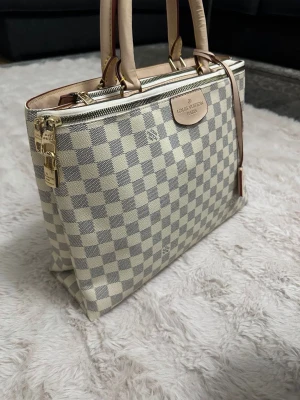 Fint handväska - Snygg handväska med beige och grå rutor. Väskan har två stabila handtag i ljust läder och guldfärgade metalldetaljer på undersidan.
