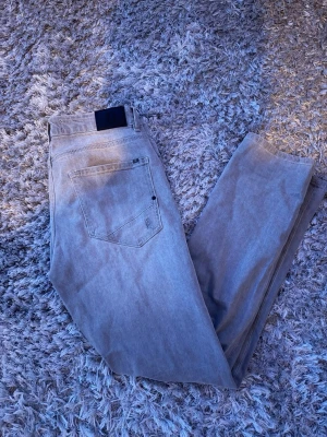 Ljusgrå jeans från Blend - Säljer ett par ljusgrå jeans från Blend med klassisk femficksdesign och diskreta slitningar framtill. Jeansen har rak passform och är tillverkade i bomullsdenim med lite stretch för extra komfort. Perfekta för en avslappnad och trendig look.