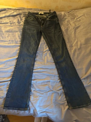 Blå bootcut jeans med låg midja - Säljer ett par klassiska blå bootcut jeans med låg midja från Zara. Jeansen har en lätt tvättad look och raka, utsvängda ben. Perfekta för dig som gillar retrostil och vill ha ett par bekväma jeans i tidlös modell. Jeansen har en litet vit fläck längst ner på höger ben som man ser i bild två!