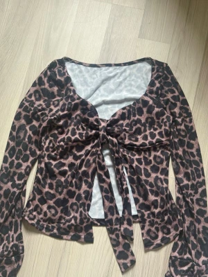 Leopardmönstrad topp med knyt - Trendig leopardmönstrad topp från SHEIN med långa ärmar och snygg knytning framtill. Toppen har en djup v-ringning och är tillverkad i ett mjukt, stretchigt material. Endast provad.