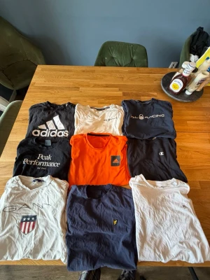 9-pack t-shirts från alla möjliga ställen. - Säljer ett paket med 9 t-shirts från märken som Adidas, Gant, Peak Performance, Sail Racing, Champion och Lyle & Scott. Färgerna är svart, vit, marinblå och en orange träningströja . Klassiska loggor på bröstet, rund hals och korta ärmar. Perfekt bas för garderoben.jag tänker att jag säljer hela packet men om man vill ha nån enskild så är det bara att skriva, storlekarna är lite oklara man alla skulle jag säga motsvarar S kanske nån XS.