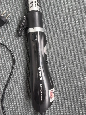 Bosch varmluftsborste svart - En svart och silverfärgad varmluftsborste från Bosch med flera knappar för olika inställningar och jonfunktion. Handtaget har ergonomisk form och borsten har ventilationshål för jämn värmefördelning. Perfekt för styling av hår och lockar.