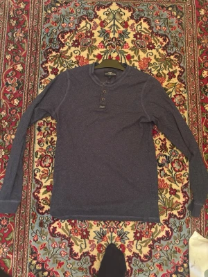 Mörkblå Henley - Mörkblå långärmad tröja/henley från Hampton republic med rund halsringning och tre knappar framtill. Perfekt för en avslappnad och snygg look. OBS: det finns ett litet hål i ena armhålet.