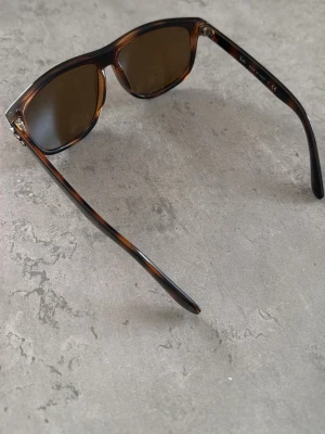 Bruna boyfriend solglasögon Ray-Ban - Snygga boyfriend solglasögon från Ray-Ban med brunt, sköldpaddsmönstrat plastbåge och mörka glas. Klassisk och tidlös design som passar till alla outfits. Ray-Ban-logga på linsen och silverdetaljer vid gångjärnen.