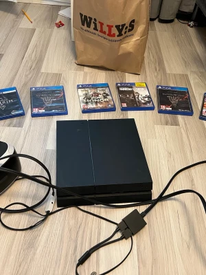 PlayStation 4 svart spelkonsol - Säljer en svart PlayStation 4 från Sony med klassisk rektangulär design. Konsolen är tillverkad i plast och har en matt finish. Medföljer kablar och flera PS4-spel i blå fodral. Perfekt för gaming och underhållning. Vr får ni oxå med. Allt funkar.