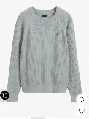 Ljusgrå stickad tröja från Gant - Ljusgrå stickad tröja från Gant med rund halsringning och diskret logga broderad på bröstet. Storleker är 13-14 år. Tröjan har ribbstickad struktur, långa ärmar och breda muddar vid ärmslut och nederkant. Perfekt för lager på lager och enkel att matcha. 